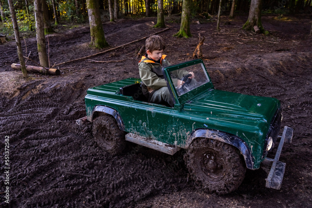 Fototapeta premium A Teen ride in an open iron children's car. Extreme form of entertainment for children. The boy drives through the mud in the forest. High quality photo