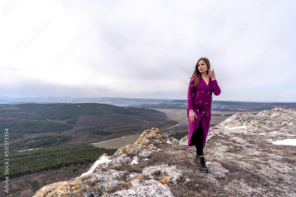 A beautiful woman stands on a high place with an amazing view of the mountains and the gorge. The concept of tourism, travel.