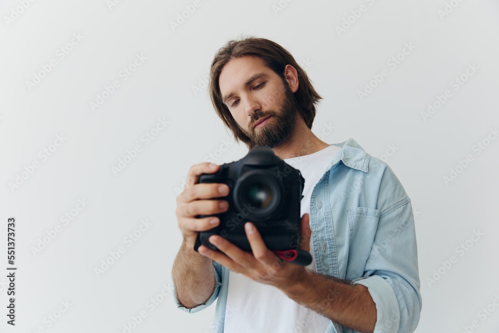 Man hipster photographer in a studio on a white background looking at the camera screen and setting it up for a photo shoot Man hipster photographer in a studio on a white background looking at the camera screen and setting it up for a photo shoot