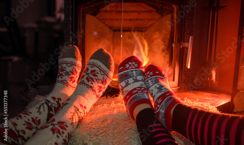 Feets in woollen socks by the Christmas fireplace. Couple sitting neat the fireplace, relaxes by warm fire and warming up their feet in woollen socks.