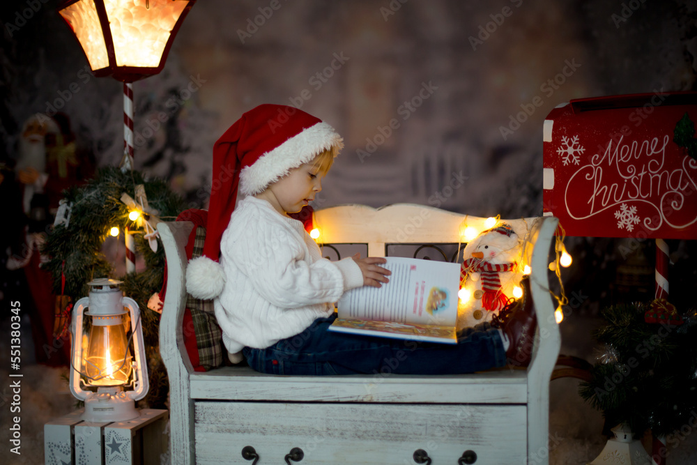 Fototapeta premium Beautiful child, reading a book, sitting on a bench with christmas decoration