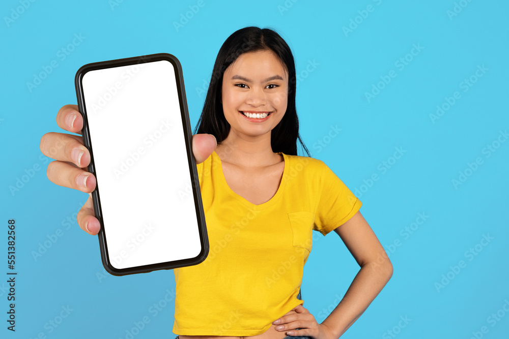 Happy millennial korean female blogger in yellow t-shirt show smartphone with empty screen Happy millennial korean female blogger in yellow t-shirt show smartphone with empty screen