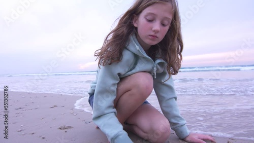 Red hair teen girl is playing with sand on the beach at sunset