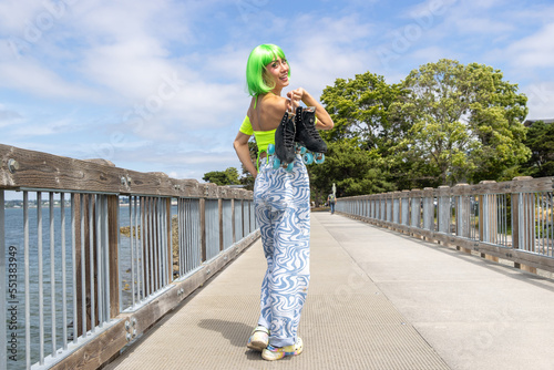 Pretty Asian woman with colorful green hair walking in waterfront park holding roller skates photo