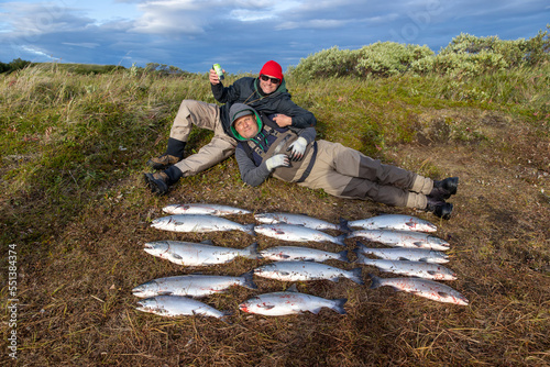 Two men, best friends smile and pose on the Alaskan tundra with a cold beer and 15 fresh caught coho salmon fish on a fishing trip in Alaska photo