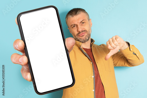 Konstfotografi Mature caucasian man showing smartphone screen and showing dislike with thumbs d