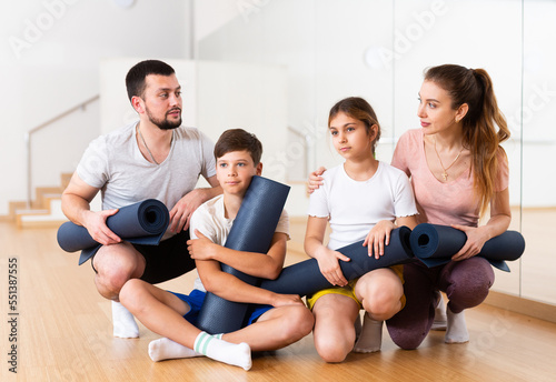 Family portrait of kids and parents with yoga mats in gym.