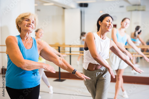 Portrait of smiling mature woman practicing ballet dance moves during group class in choreographic studio