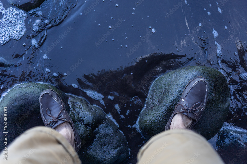 male feet in top siders on green stones over water