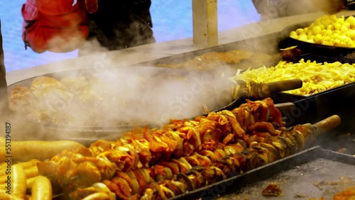 Outdoors, traditional meat dishes are cooked in a large frying pan at a street cafe at the Christmas market in Krakow, Poland. Authentic scene of Polish culinary traditions on the eve of Christmas