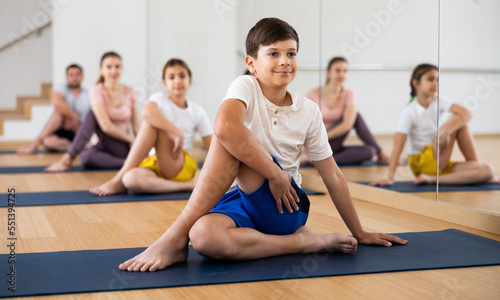 Young boy exercising lord of the fishes pose with her family during group yoga training.