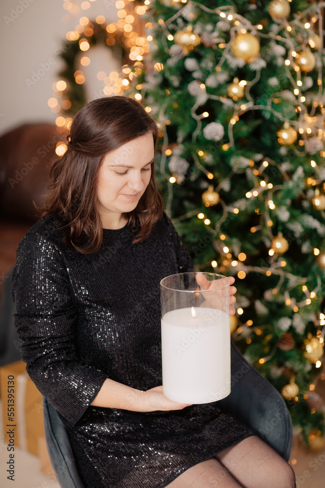 Φωτογραφία Woman in black glitter dress holding candle and sitting near Christmas tree