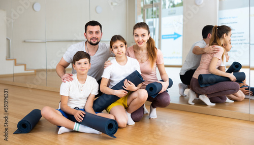 Fototapeta Naklejka Na Ścianę i Meble -  Cheerful friendly sporty young parents with teen daughter and son posing with gymnastic mats before exercising in yoga class