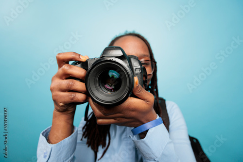 Amateur photographer taking photos with modern DSLR device while standing on blue background. Photography entusiast enjoying taking pictures with photo camera. Studio shot photo