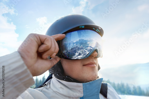  Man on the background blue sky. Wearing ski glasses. Winter Sports. Close up of the ski goggles of a man with the reflection of snowed mountains
