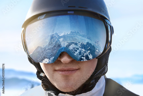 Ski Goggles With The Reflection Of Snowed Mountains. Man On The Background Blue Sky. Winter Sports