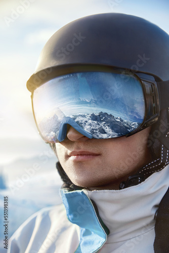 Portrait of man on the background blue sky holds ski goggles with the reflection of snowed mountains..Winter Sports