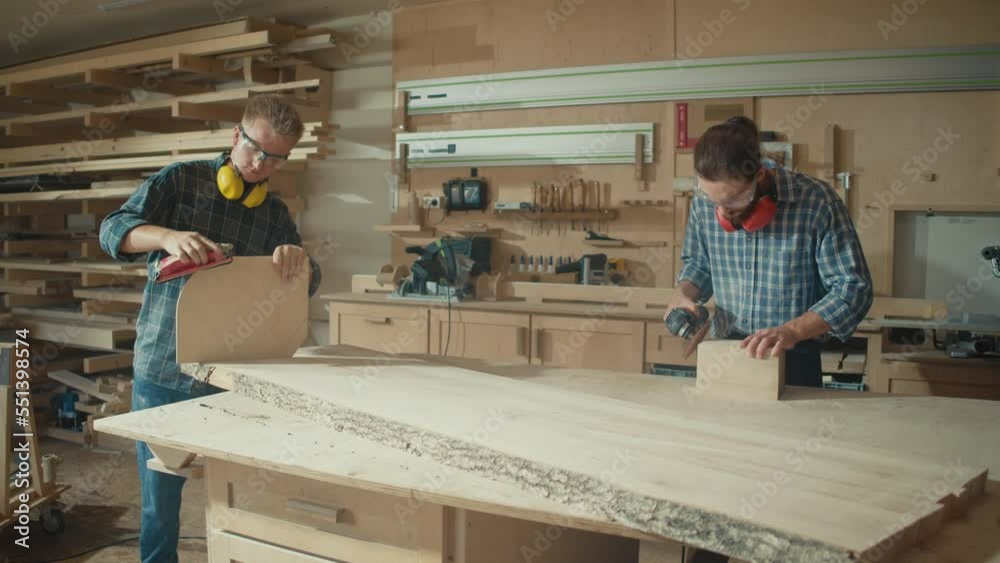 Carpenters Working With Hand and an Electric Sander to Sanding a Wooden Plank in a Woodworking Workshop. Manual Labor. Carpentry, Craftsmanship, and Handwork Concept. Carpenters Working With Hand and an Electric Sander to Sanding a Wooden Plank in a Woodworking Workshop. Manual Labor. Carpentry, Craftsmanship, and Handwork Concept.