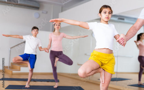 Girl standing in tree pose during group yoga training with her family in fitness studio.