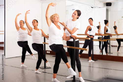 Female ballet trainer teaching group of multiracial dancers near ballet barre in dancing hall