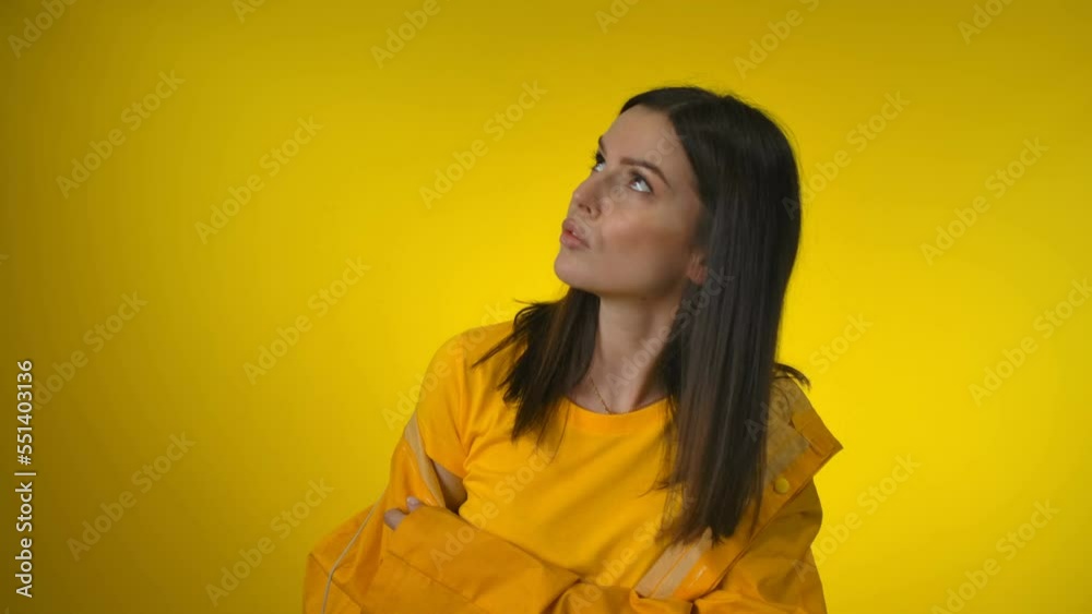 Sad attractive woman in a bright yellow raincoat is worried and looking up Sad attractive woman in a bright yellow raincoat is worried and looking up