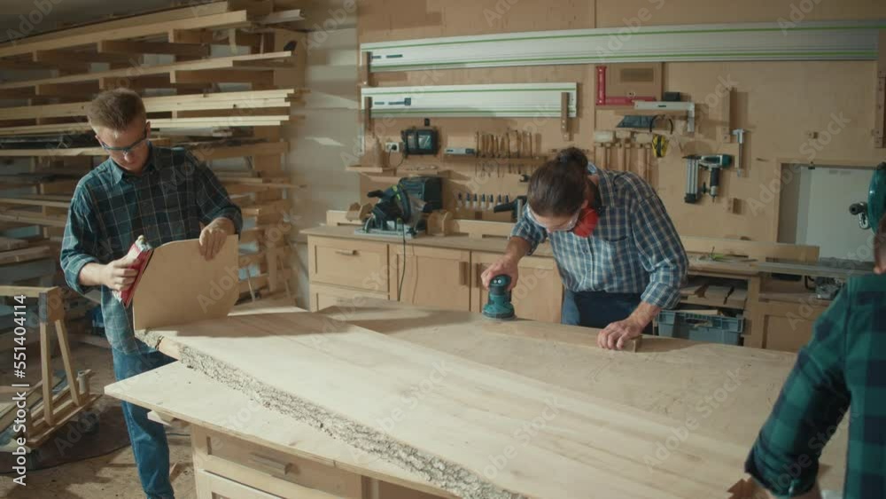 Carpenters Working With Hand and an Electric Sander to Sanding a Wooden Plank in a Woodworking Workshop. Manual Labor. Carpentry, Craftsmanship, and Handwork Concept. Carpenters Working With Hand and an Electric Sander to Sanding a Wooden Plank in a Woodworking Workshop. Manual Labor. Carpentry, Craftsmanship, and Handwork Concept.
