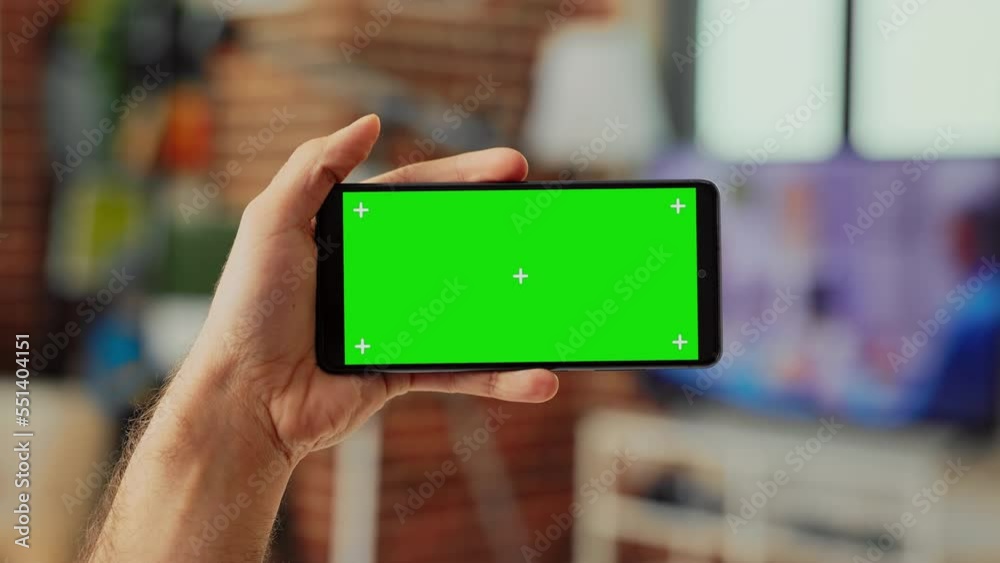 Young manager holding telephone with horizontal greenscreen template on digital screen, looking at isolated display. Using blank chroma key copyspace and mockup on smartphone. Close up. Young manager holding telephone with horizontal greenscreen template on digital screen, looking at isolated display. Using blank chroma key copyspace and mockup on smartphone. Close up.