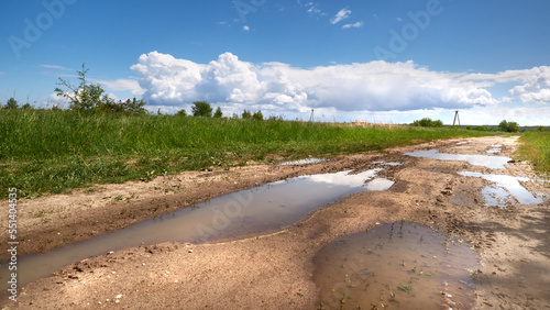 Puddles on a rural road in Poland. Sunny day with blue sky and heavy clouds. Muddy, sloshy, slippery road in Polish countryside.