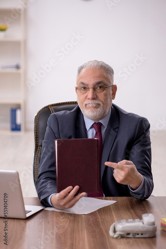 Old male boss reading book at workplace