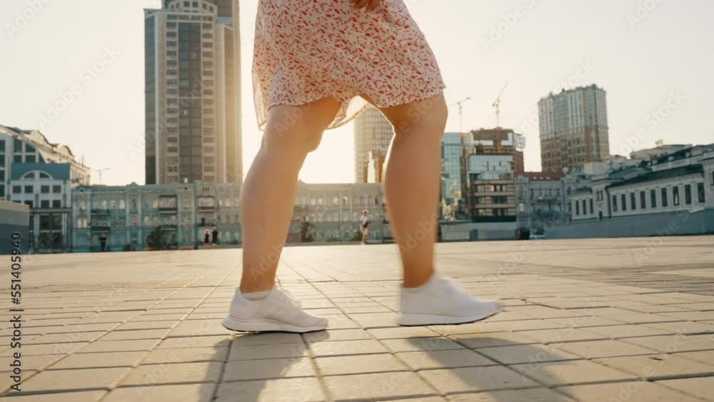 Womens legs in white sneakers are walking along the city street.