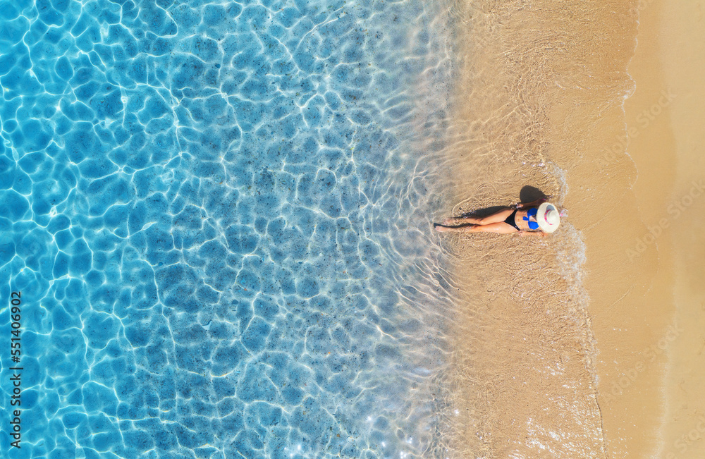 Aerial view of a lying woman in white hat on sandy beach and blue sea ...