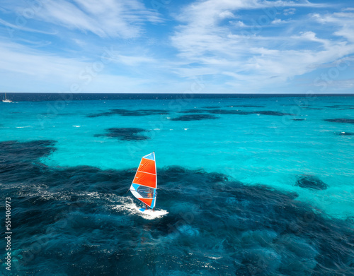 Aerial view of windsurfer on blue sea at sunny summer day. Windsurfing. Extreme sport and vacation. Top view of man on windsurfer board, waves, clear azure water in Sardinia, Italy. Tropical landscape