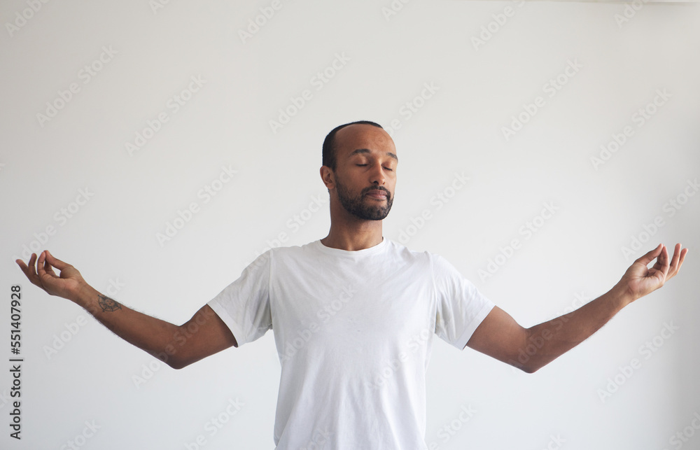 Portrait of relaxed bearded man wearing white casual style T-shirt, standing with raised arms and doing yoga meditating exercise.