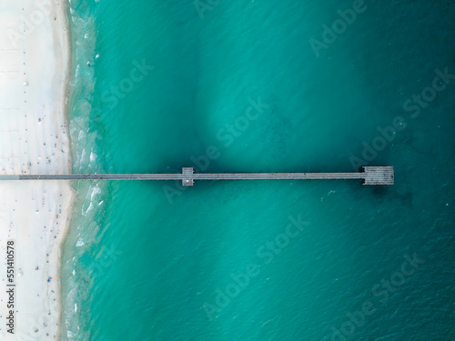 Aerial top down view of wooden pier and white sandy beach in Florida.