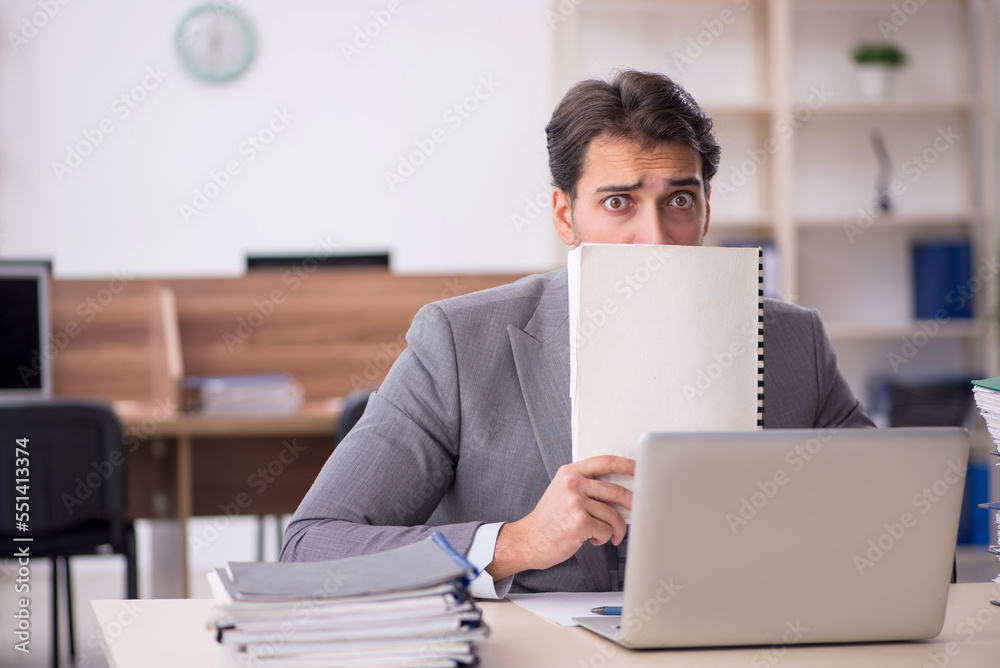 Young male employee unhappy with excessive work in the office Young male employee unhappy with excessive work in the office