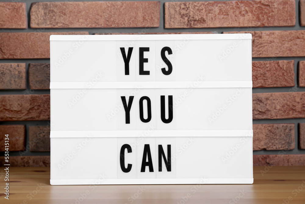 Fotografie Lightbox with phrase Yes You Can on table against brick wall