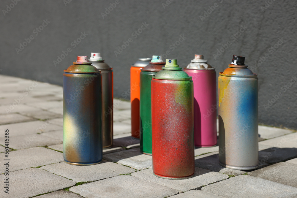 Cans of different spray paints on pavement near wall - obrazy, fototapety, plakaty 