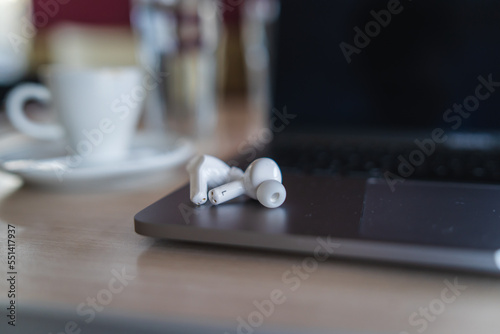 Close up of wireless earbuds on laptop on table in cafe  photo