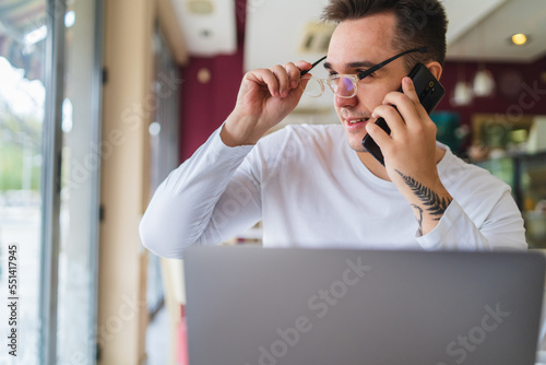 A young businessman in cafe using his laptop mobile phone and wireless earbuds while working on his project business on his laptop and talking on the phone 