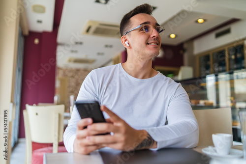 A young businessman in cafe using his laptop mobile phone and wireless earbuds while working on his project business on his laptop and talking on the phone 