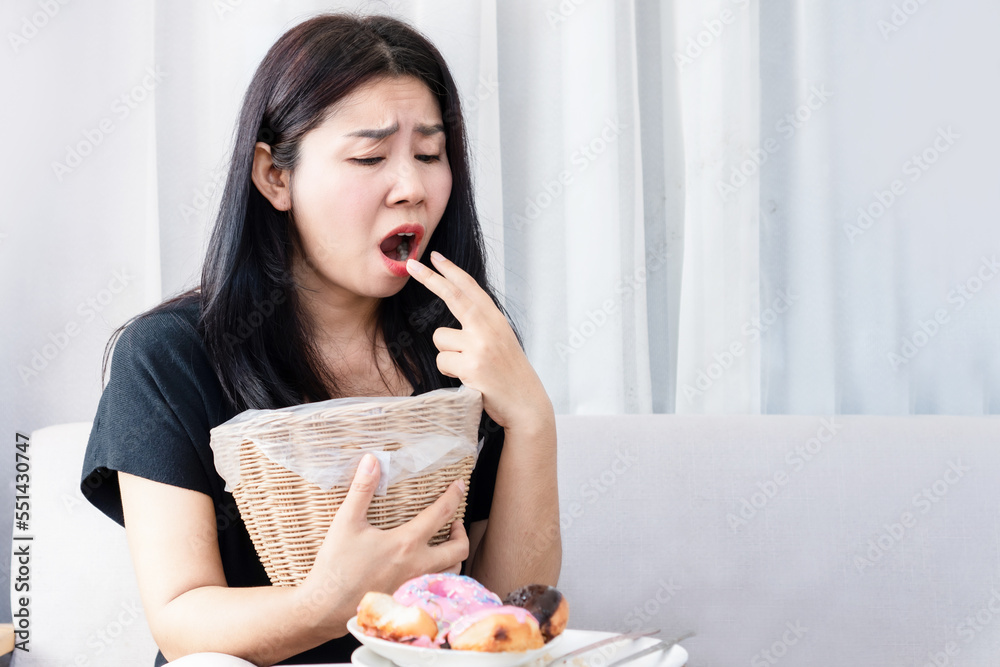 Bulimia nervosa, anorexia nervosa concept with Asian woman put her fingers in her mouth and holding bin in hand try to vomit after eating food Bulimia nervosa, anorexia nervosa concept with Asian woman put her fingers in her mouth and holding bin in hand try to vomit after eating food