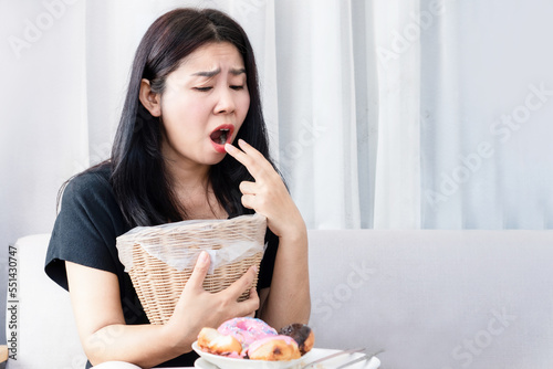 Bulimia nervosa, anorexia nervosa concept with Asian woman put her fingers in her mouth and holding bin in hand try to vomit after eating food photo