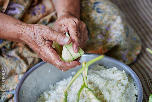 Hands of senior woman wrapping the sticky rice with palm leaf or Ketupat Palas photo