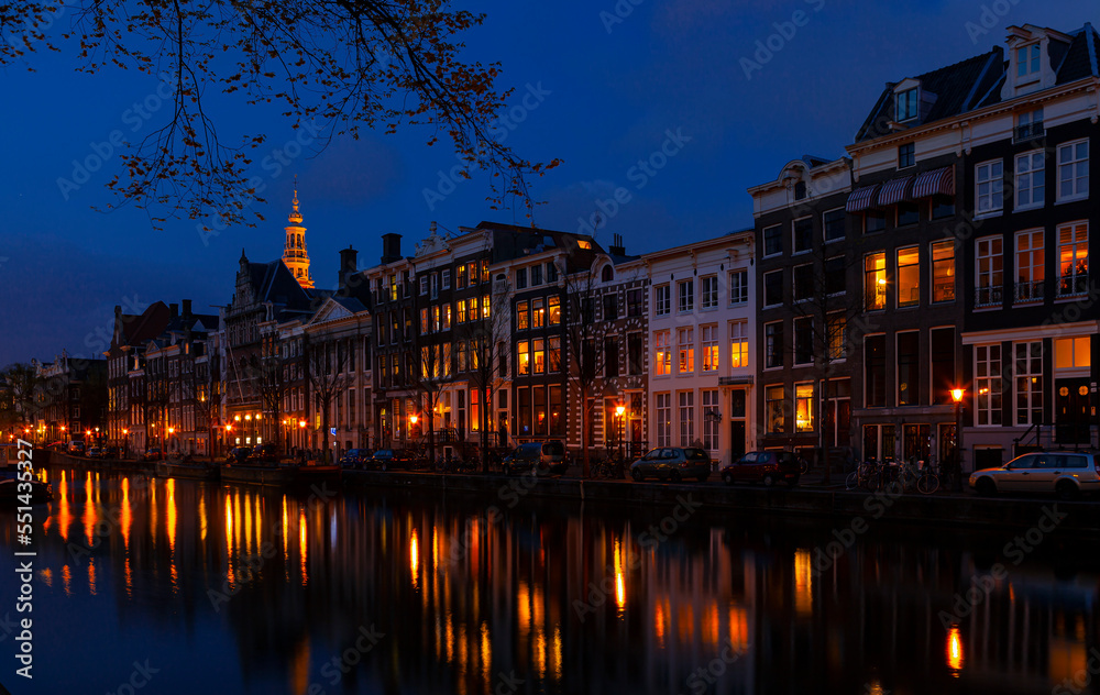 Romantic nocturnal view of Amsterdam: canal in the Red District. Buildings, cars and boats are reflected in the water