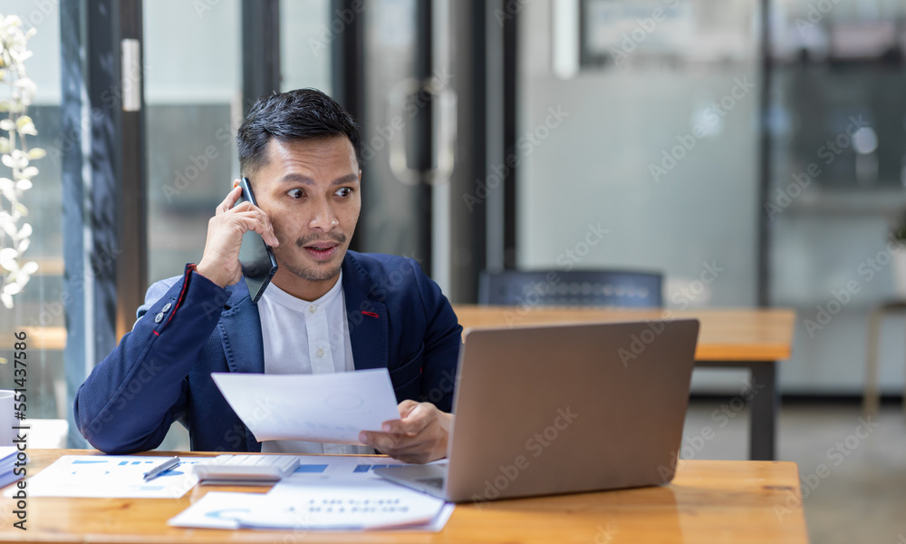 Young business Asian man working at workplace with laptop and papers on desk and using phone. Young business Asian man working at workplace with laptop and papers on desk and using phone.
