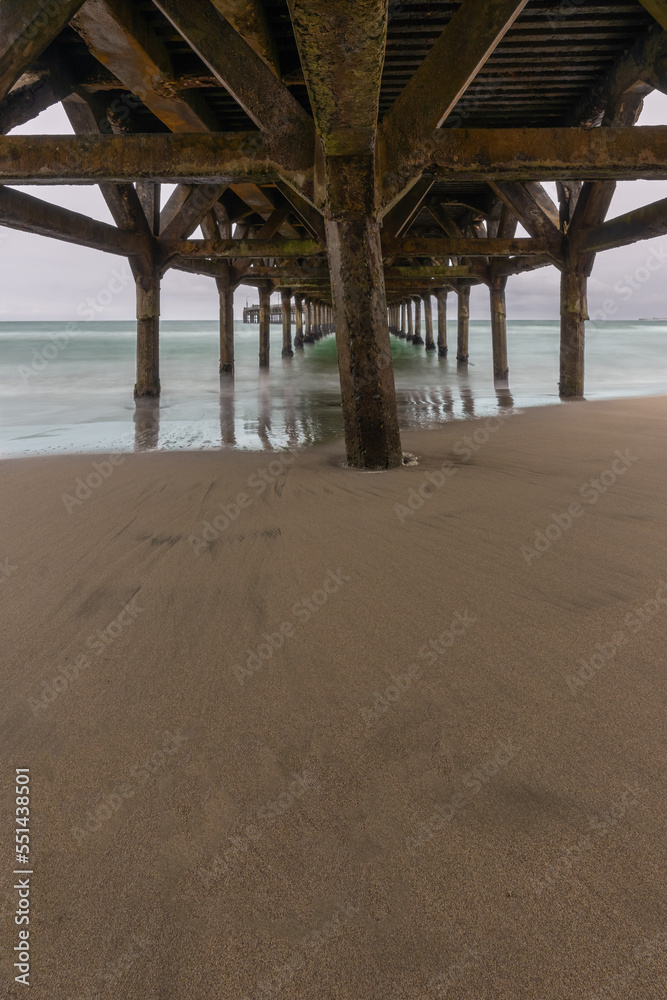 Under a concrete pier on a sandy beach, during a cloudy day.