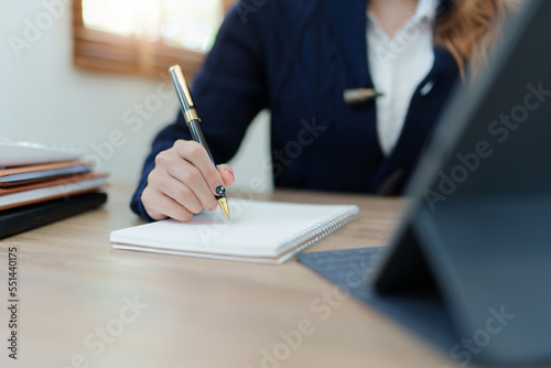 Portrait of a young Asian man showing a smiling face as she uses his notebook, tablet computer and financial documents on her desk in the early morning hours