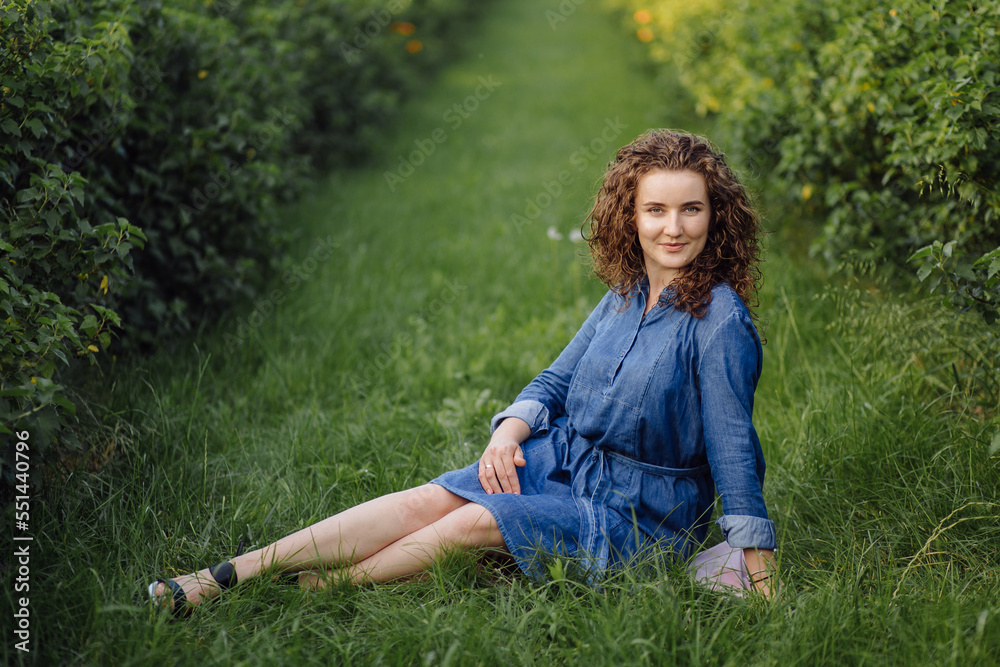 Happy young woman with brown curly hair, wearing a dress, posing outdoors in a garden Happy young woman with brown curly hair, wearing a dress, posing outdoors in a garden