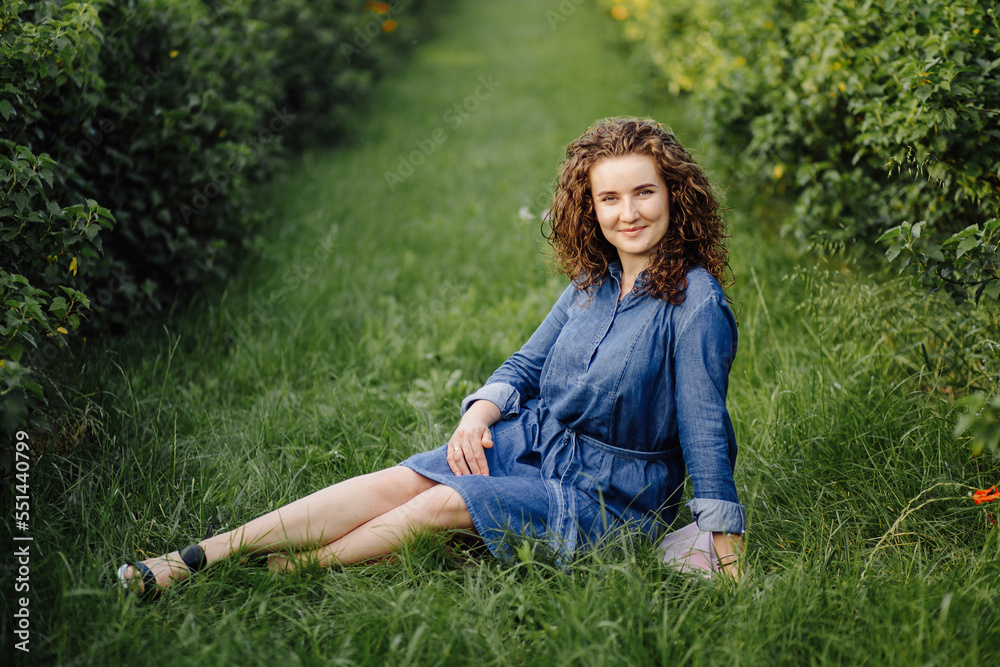 Happy young woman with brown curly hair, wearing a dress, posing outdoors in a garden Happy young woman with brown curly hair, wearing a dress, posing outdoors in a garden