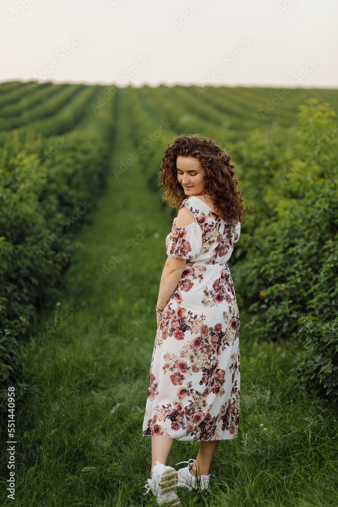 Happy young woman with brown curly hair, wearing a dress, posing outdoors in a garden Happy young woman with brown curly hair, wearing a dress, posing outdoors in a garden